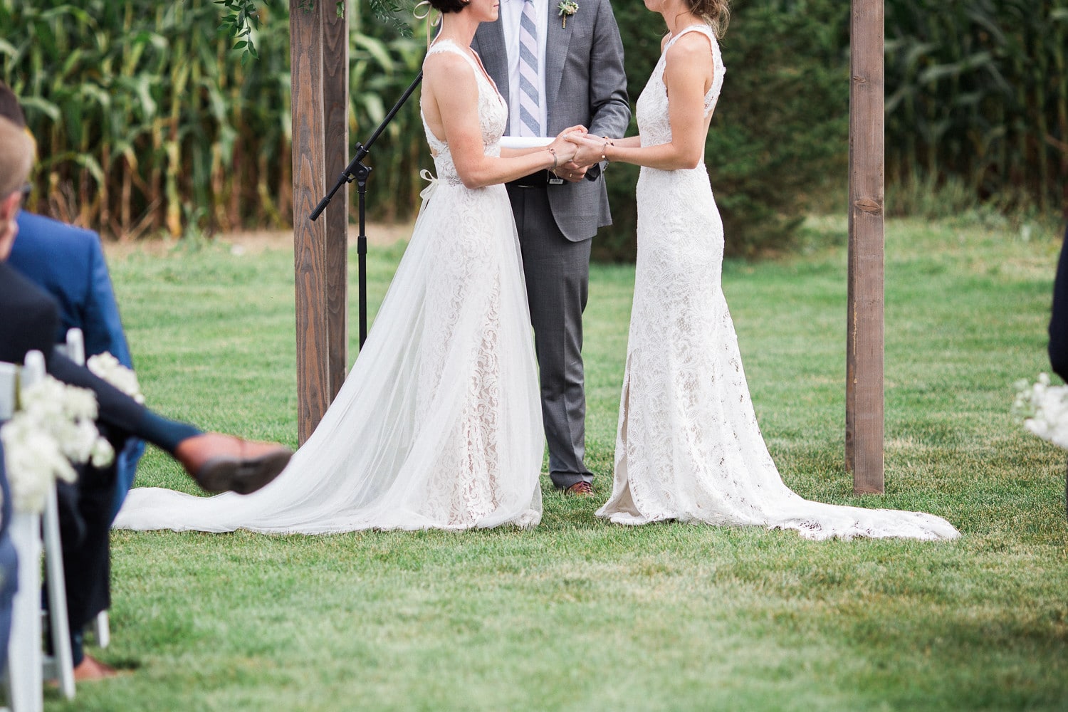 Two women in white dresses holding hands during wedding ceremony